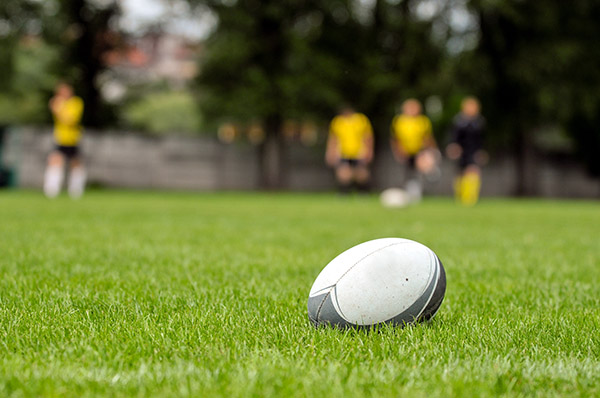 a white rugby ball on the green grass of a rugby pitch with some players wearing yellow in the distance a white rugby ball on the green grass of a rugby pitch with some players wearing yellow in the distance