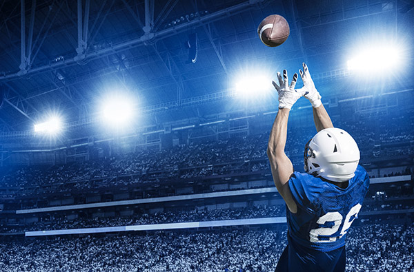 Alt text: packed stadium at nighttime with an American football player catching the ball in the foreground Alt text: packed stadium at nighttime with an American football player catching the ball in the foreground
